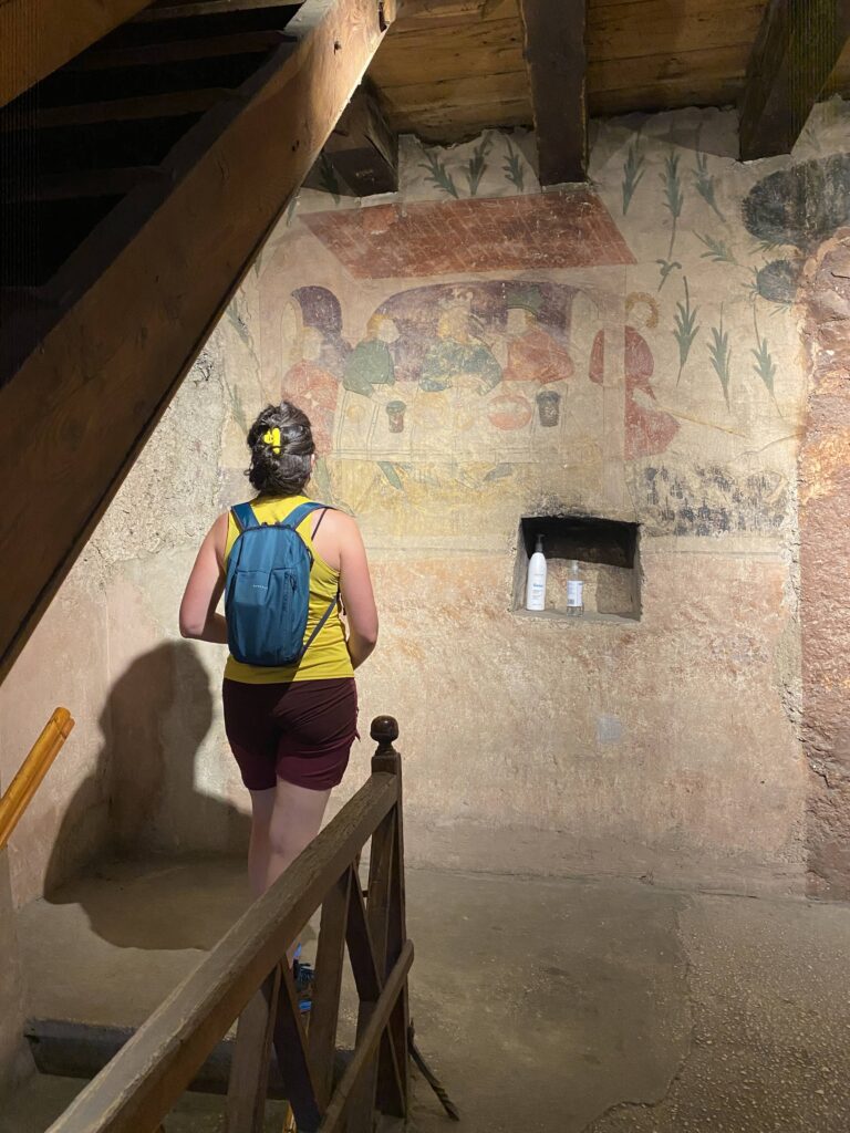 Una persona guarda le pitture murali interne a Palazzo Nero. I colori sono sbiaditi ma si possono ancora vedere bene le figure sedute intorno a un tavolo