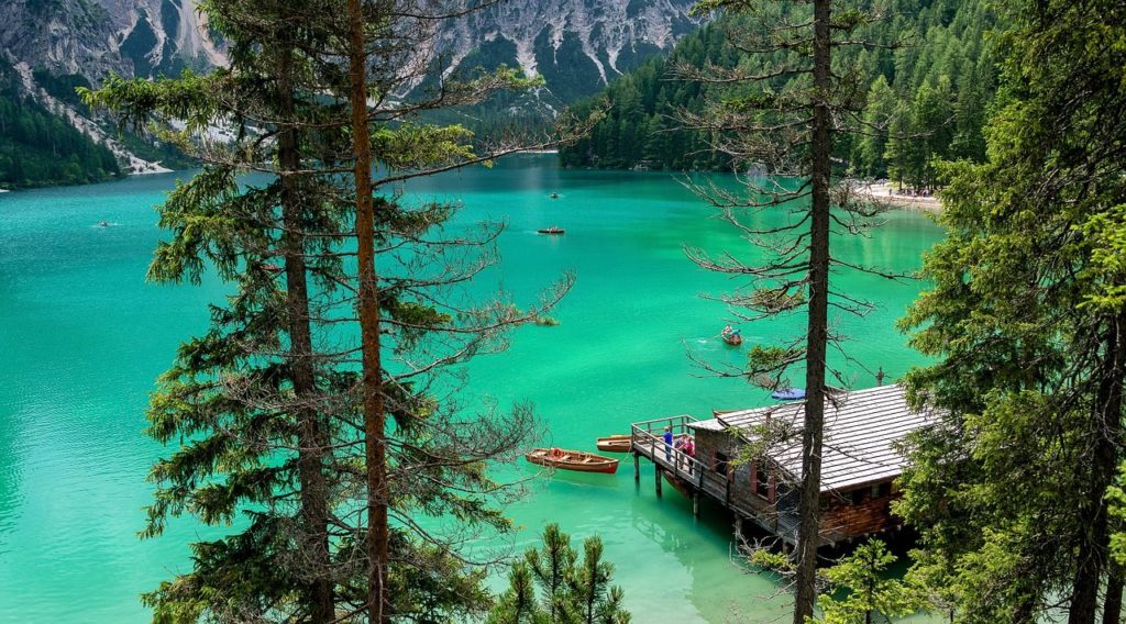 Scorcio del lago di Braies da un'altezza media, so scorge l'acqua verde tra gli abeti, la casetta delle barche e due barche ormeggiate