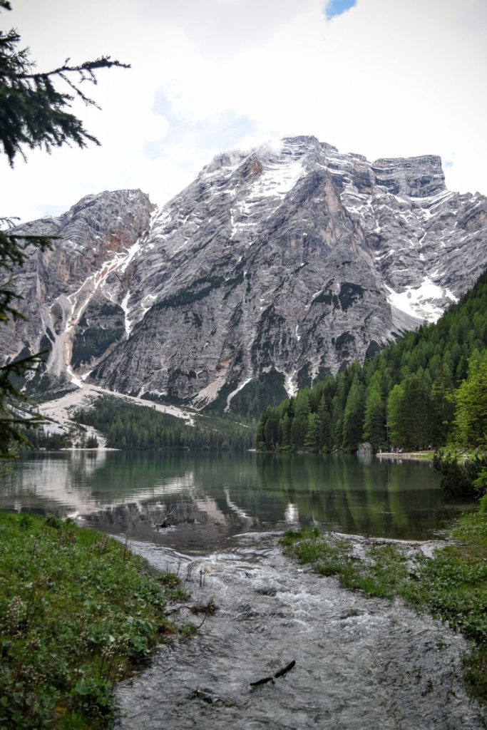 Vista del lago di Braies con la montagna di rocce sullo sfondo dove ancora si può vedere la neve nei punti più ombreggiati della montagna, la Croda del Becco. In primo piano l'acqua verde e i pini