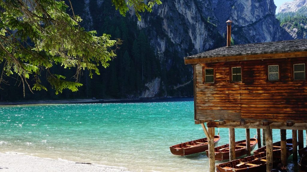 Uno scorcio ravvicinato della casetta delle barche sul lago di Braies, l'acqua azzurro-verde, qualche barchetta ormeggiata e un ramo d'abete in primo piano sulla sinistra